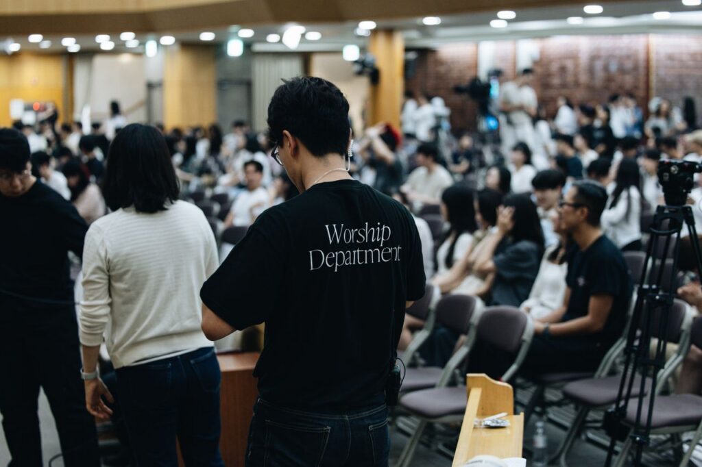 Crowd attending a church service with worship team preparing in the foreground.