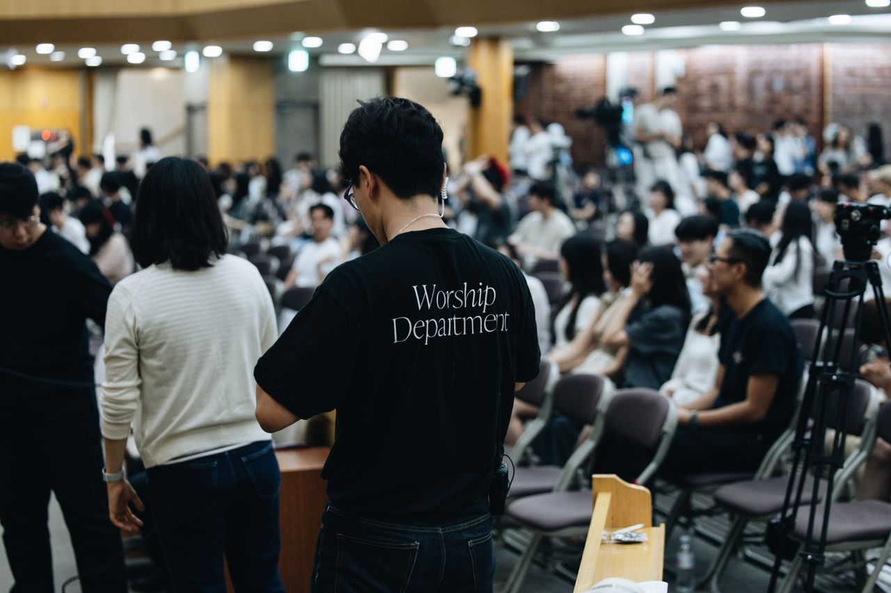 Crowd attending a church service with worship team preparing in the foreground.