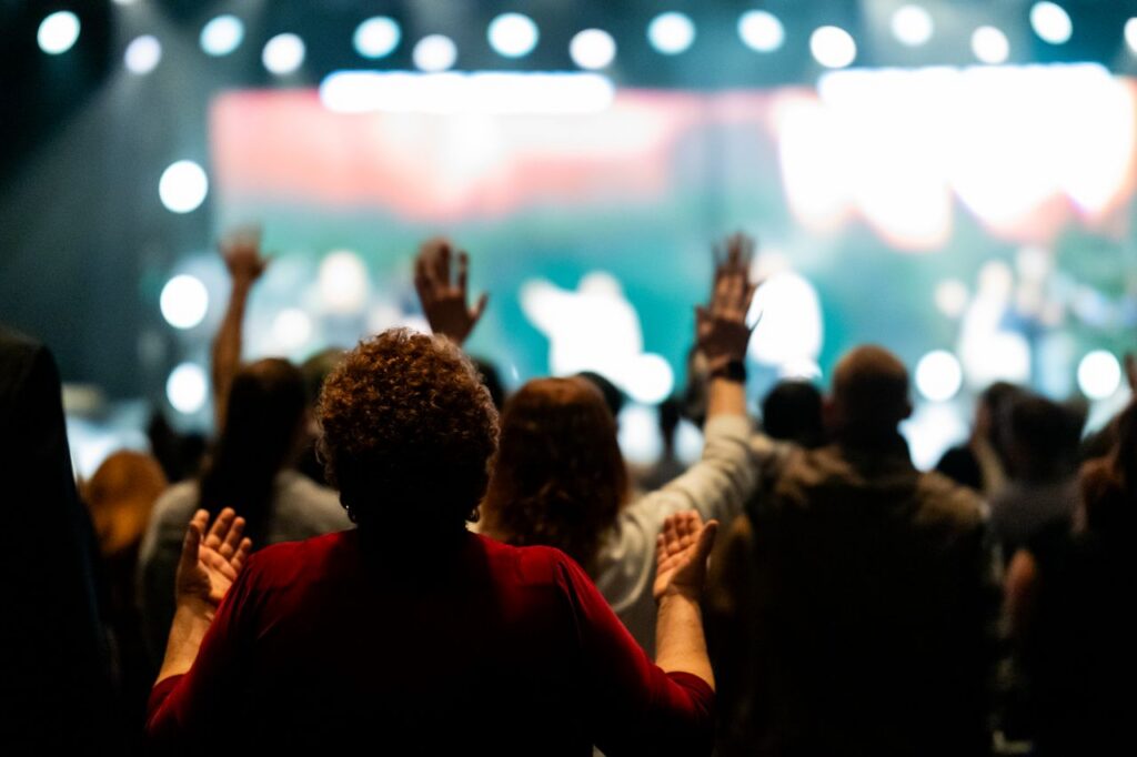 A diverse group of people worshiping with raised hands at an indoor event.